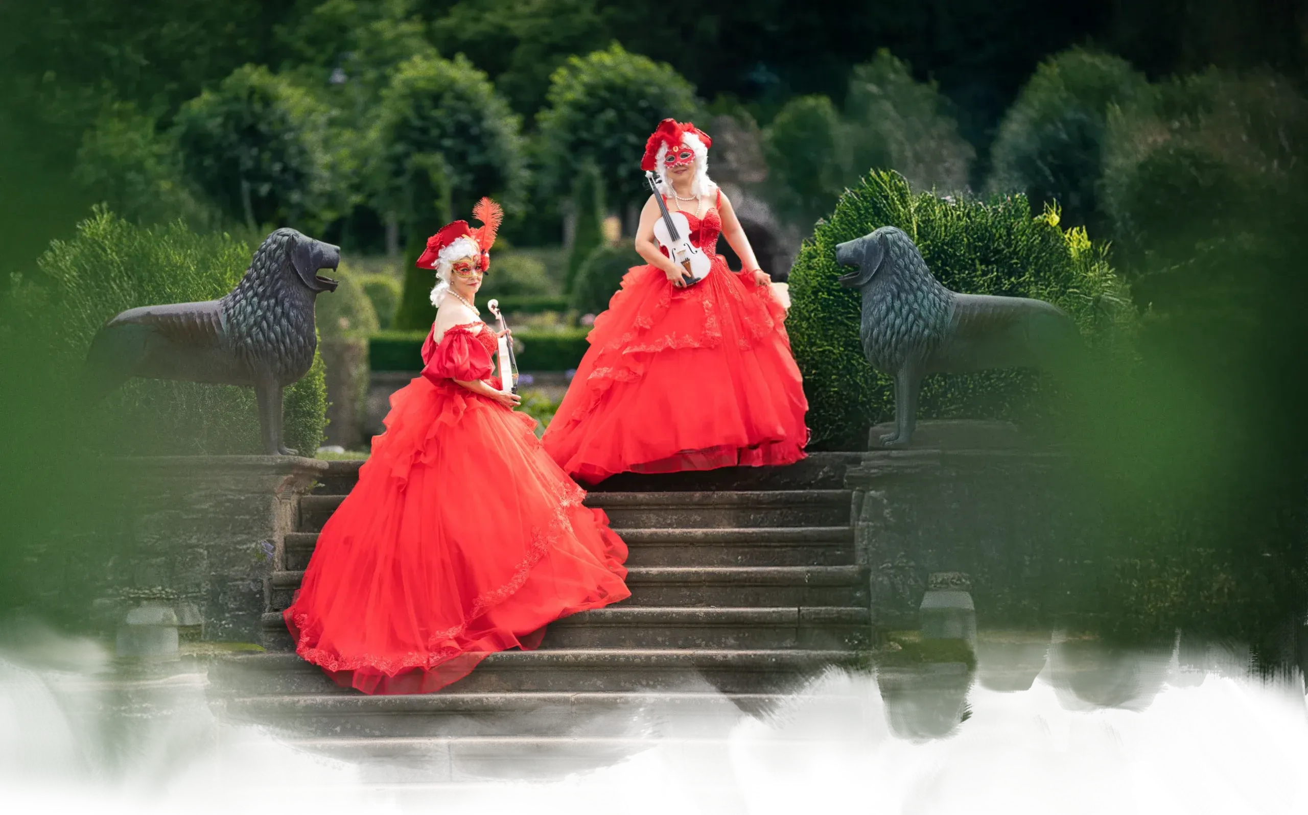 Zwei Frauenmit opulenten, roten Kleidern mit Geigen auf Treppe