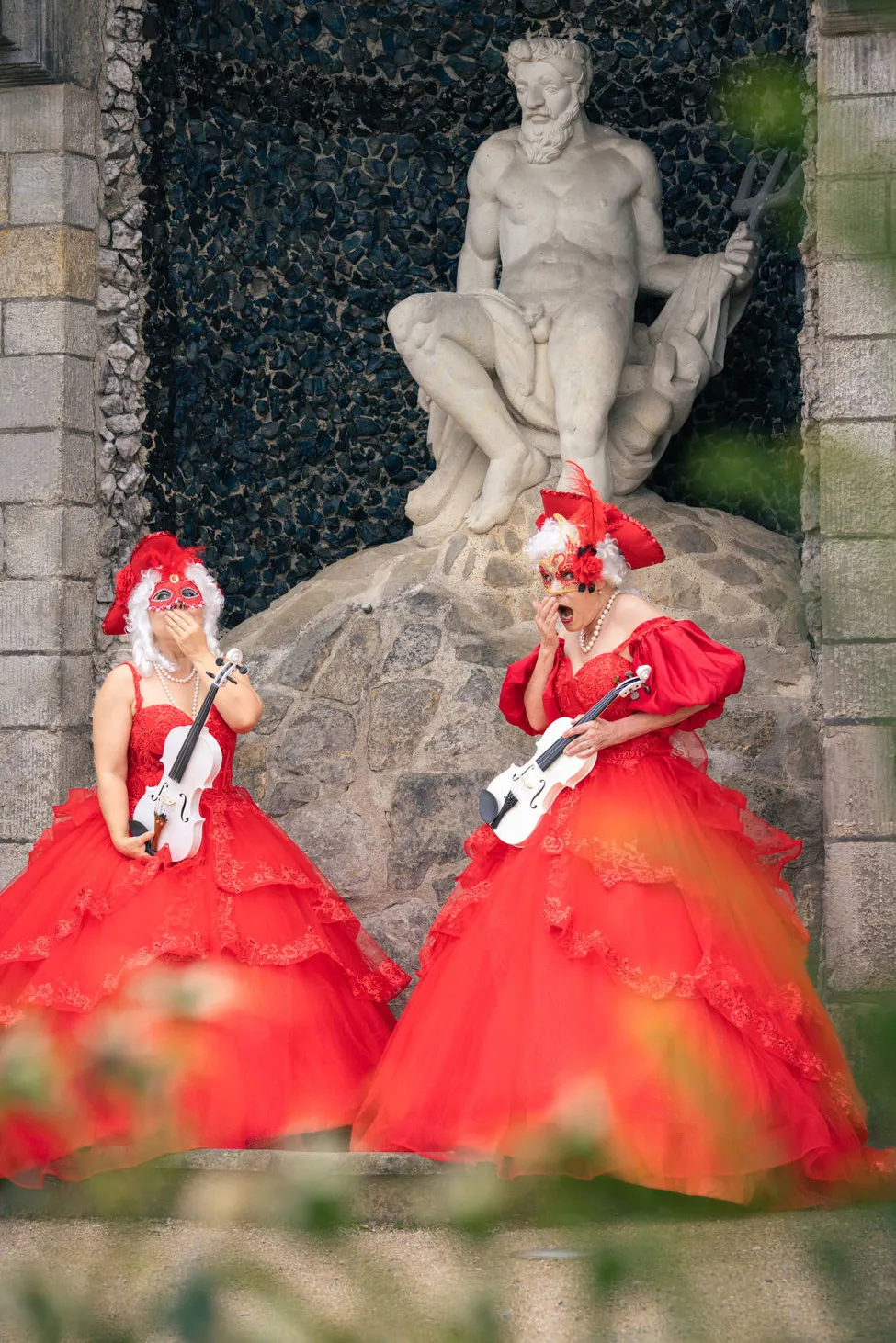 Zwei Frauenmit opulenten, roten Kleidern mit Geigen auf Treppe